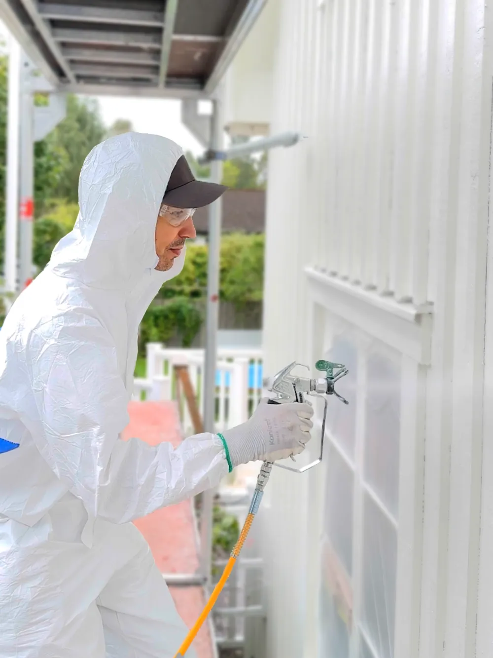 Målare hos SAVL Solutions i vit skyddsdräkt sprutlackerar träfasad vit från byggställning.