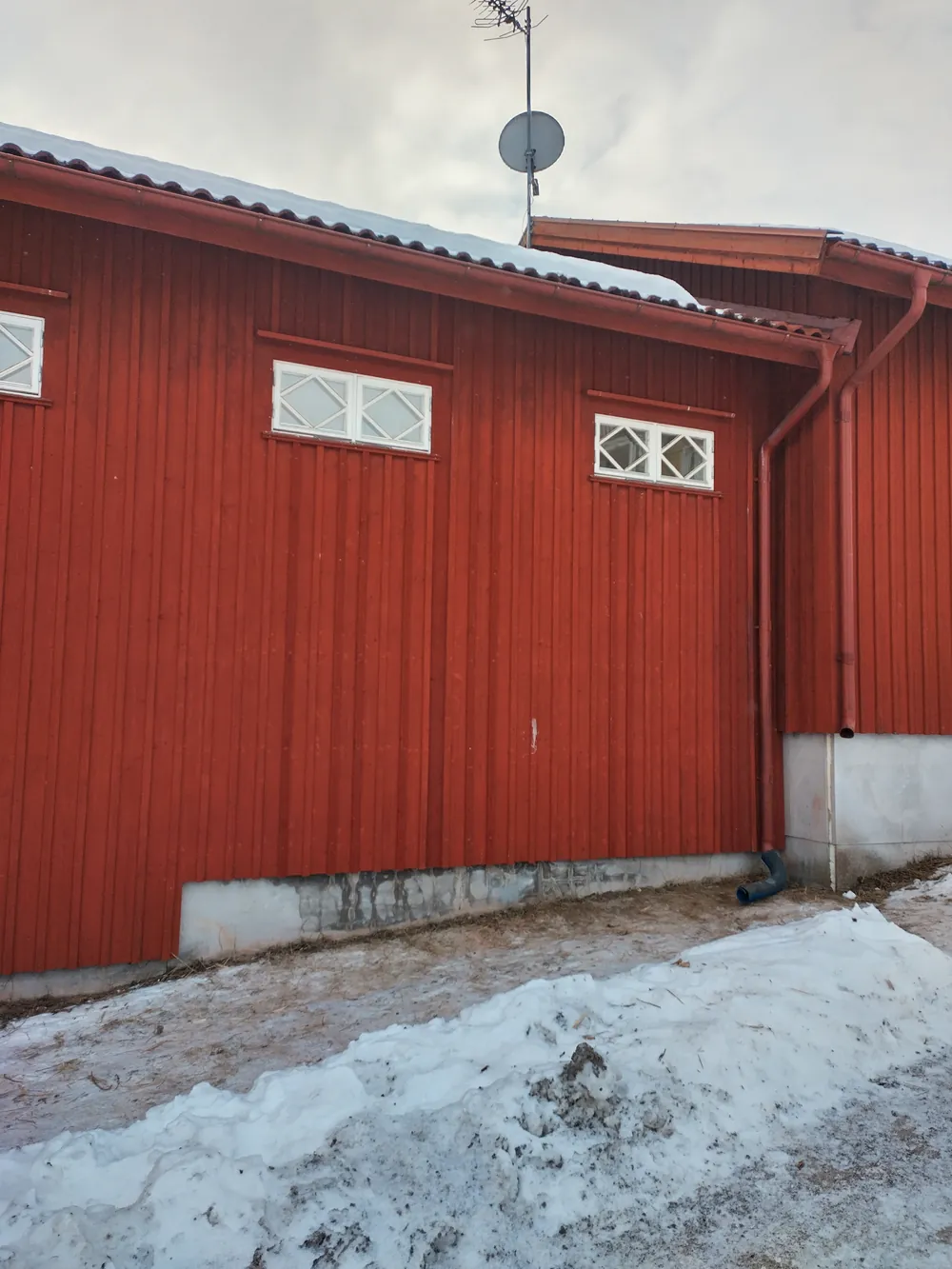 Röd träfasad nymålad med traditionell rödfärg och vita fönsterfoder. Utvändig renovering av hus och plåtdetaljer i vintermiljö.
