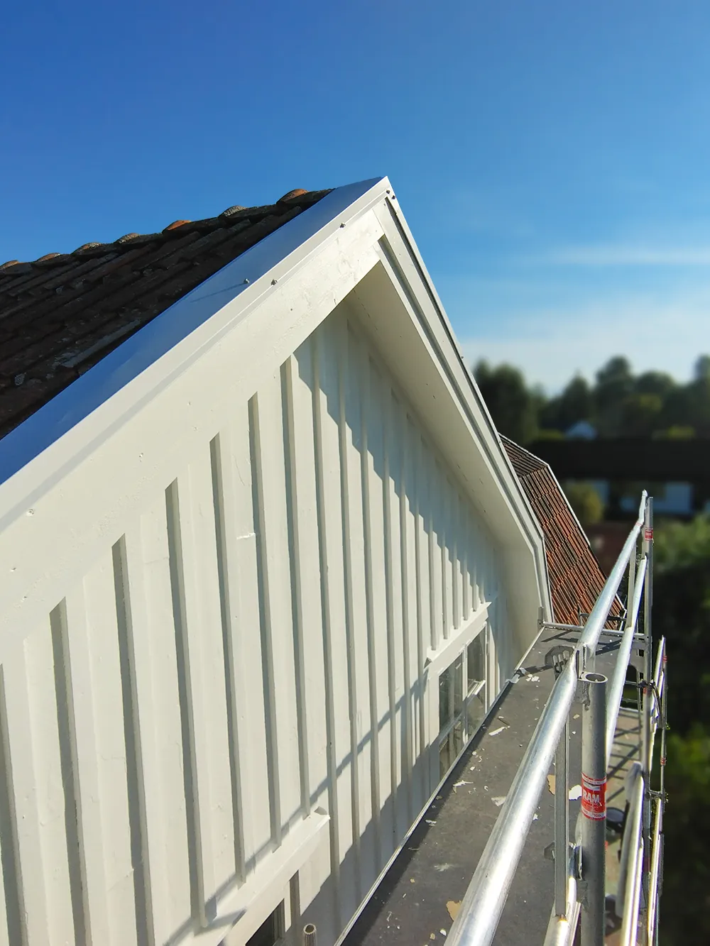 NAVL Solutions har nymålat vit träfasad och gavel på hus med byggställning under solig dag.