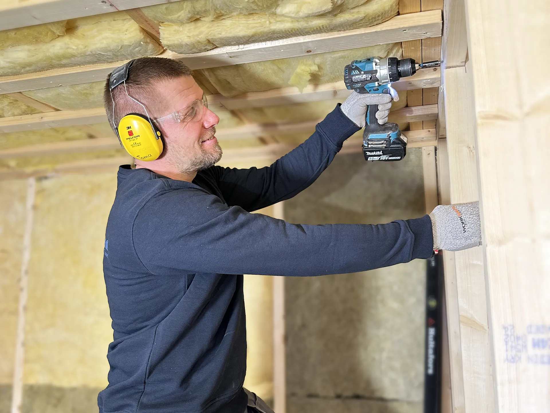 Snickare från SAVL Solutions monterar reglar vid isolering av tak och väggar. Professionellt byggarbete utförs med skruvdragare och skyddsutrustning vid renovering.