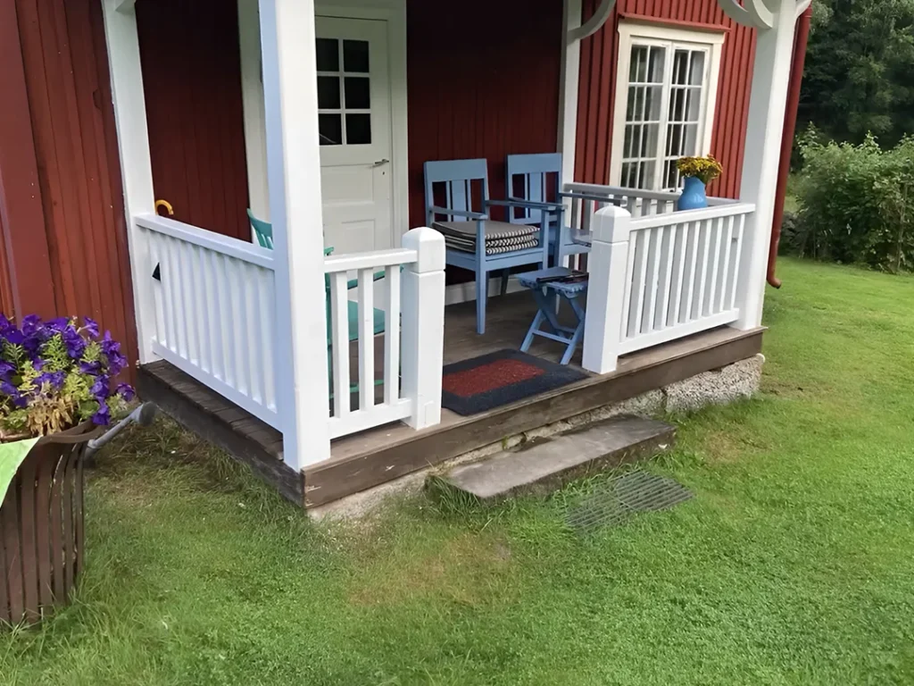 Färdigrenoverad veranda med nytt vitt räcke och trädetaljer efter snickeriarbete i Karlstad