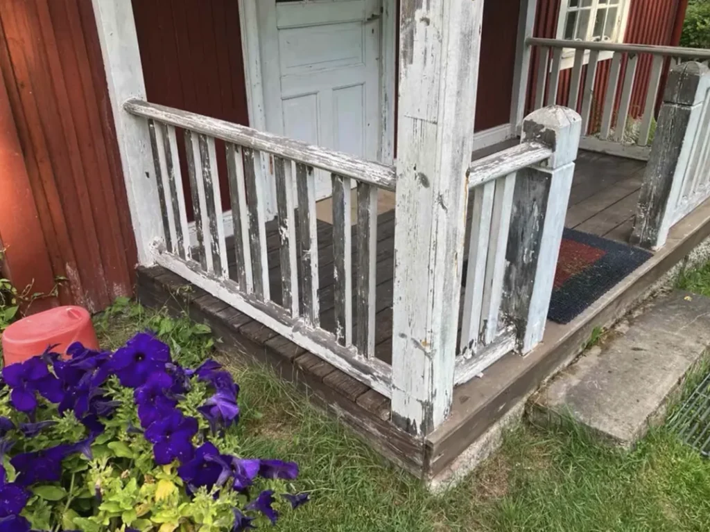 Sliten veranda före renovering med gammalt träräcke och trall vid rött trähus i Karlstad